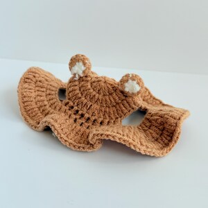 May include: A brown crocheted hat with white bear ears. The hat has a wide brim and is designed for a small pet.