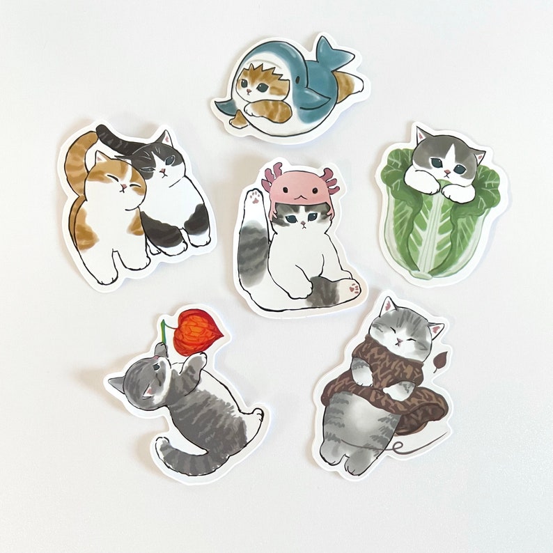May include: Set of nine stickers featuring cute cartoon cats in various poses and outfits. The stickers are printed on white paper and have a glossy finish.