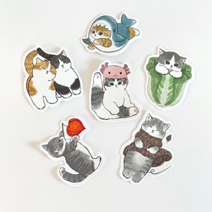 以下が含まれることがあります： さまざまなポーズと衣装を着たかわいい漫画の猫が描かれた9枚のステッカーのセット。ステッカーは白い紙に印刷されており、光沢のある仕上げになっています。