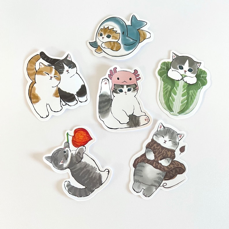 以下が含まれることがあります： さまざまなポーズと衣装を着たかわいい漫画の猫が描かれた9枚のステッカーのセット。ステッカーは白い紙に印刷されており、光沢のある仕上げになっています。