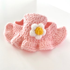 May include: A pink crocheted flower-shaped dog collar with a white flower and yellow center.