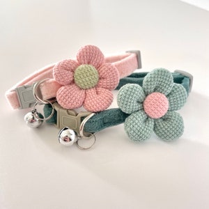 May include: Two cat collars with flower details. One is pink with a light green centre, the other is green with a pink centre. Both have silver bells and grey buckles.