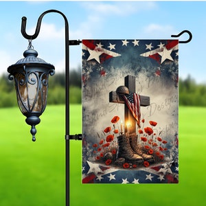 May include: A garden flag featuring a wooden cross draped with an American flag and a military helmet. Combat boots rest at the base, surrounded by red poppies. The background has a patriotic design with stars and stripes.