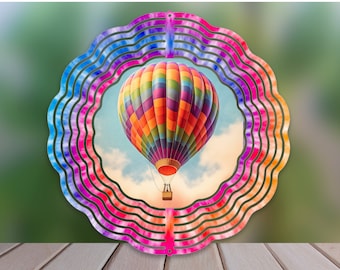 May include: A colorful metal wind spinner with a rainbow design and a hot air balloon in the center. The balloon is red, orange, yellow, green, blue, and purple.
