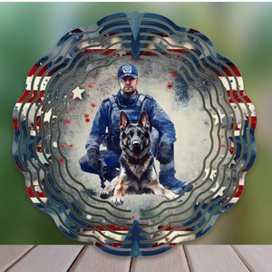 May include: A metal wind spinner with a patriotic design featuring a police officer and a German Shepherd dog. The spinner has a circular shape with multiple layers of red, white, and blue stripes.