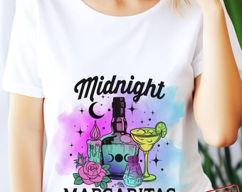May include: A white t-shirt with a colourful design featuring a bottle of tequila, a margarita glass, a candle, and a salt shaker. The text "Midnight Margaritas" is printed in black on the shirt.