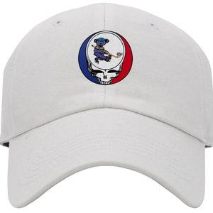 May include: White baseball cap with a colorful embroidered patch featuring a cartoon bear playing hockey. The patch is a circular design with a skull and crossbones in the center.
