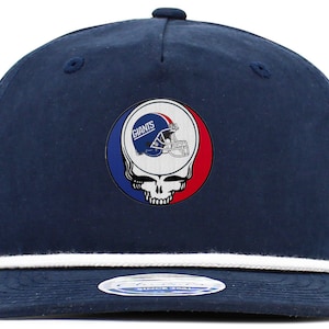 May include: A navy blue baseball cap with a white rope trim. The front of the cap features a red, white, and blue circular patch with a skull and crossbones design and the words "Giants" in white.