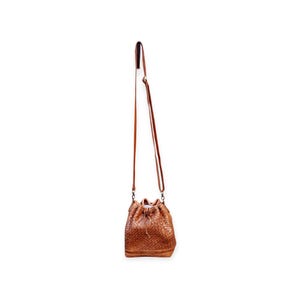 Puede incluir: Un bolso tipo cubo de cuero marr&oacute;n con una textura tejida. El bolso tiene una correa larga y ajustable para llevarlo cruzado. El bolso est&aacute; suspendido sobre un fondo blanco.
