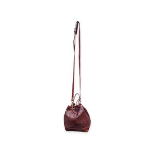 Puede incluir: Un bolso tipo cubo de cuero marr&oacute;n con una correa larga y delgada para el hombro. El bolso tiene una textura tejida y un cierre de cord&oacute;n. La correa est&aacute; sujeta al bolso con herrajes met&aacute;licos.