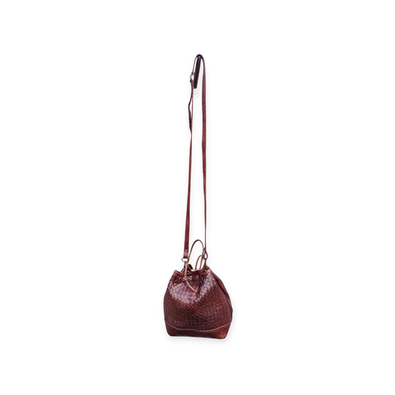 Puede incluir: Un bolso tipo cubo de cuero marr&oacute;n con una correa larga y delgada para el hombro. El bolso tiene una textura tejida y un cierre de cord&oacute;n. La correa est&aacute; sujeta al bolso con herrajes met&aacute;licos.