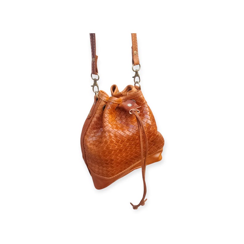 Puede incluir: Bolso tipo cubo de cuero tejido marr&oacute;n. Cuenta con cierre de cord&oacute;n y una correa larga y ajustable. El bolso presenta un patr&oacute;n de tejido de cesta y cierres met&aacute;licos. Tono c&aacute;lido y terroso.