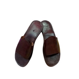 May include: A pair of brown leather sandals. The sandals have a simple design with a strap across the top and a stitched sole. The leather is a rich, dark brown color.