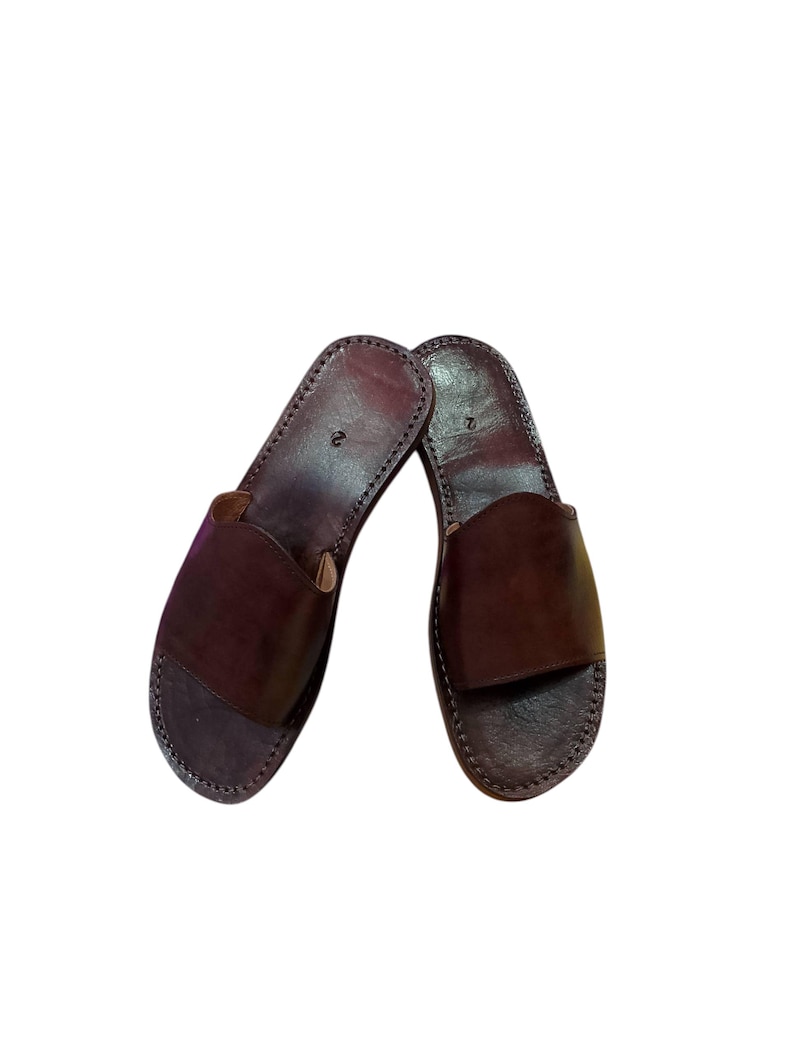 May include: A pair of brown leather sandals. The sandals have a simple design with a strap across the top and a stitched sole. The leather is a rich, dark brown color.