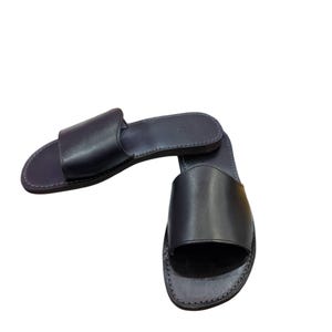 May include: A pair of black leather slide sandals. The sandals have a simple design with a single strap across the top of the foot and a flat sole. The leather appears smooth and the sandals are new.