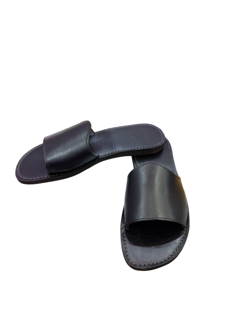 May include: A pair of black leather slide sandals. The sandals have a simple design with a single strap across the top of the foot and a flat sole. The leather appears smooth and the sandals are new.
