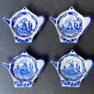 Op de afbeelding: Set van vier blauwe en witte keramische theepotvormige theezakjeshouders met een windmolen en het woord "Holland" op elk.