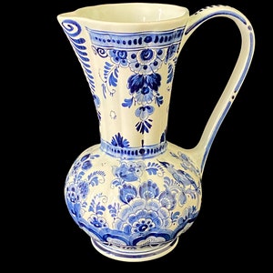 Può includere: Un'anfora in ceramica bianca con un motivo floreale blu e bianco. L'anfora ha un'ampia apertura e un manico.