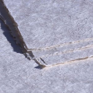 Può includere: Primo piano di carta fatta a mano con una superficie strutturata bianco sporco. La carta ha un bordo a strappo e fibre visibili, che suggeriscono una qualità naturale e artigianale. La carta è a strati, con il foglio superiore parzialmente strappato.