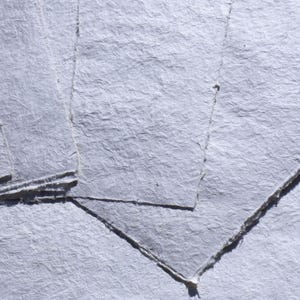 Könnte beinhalten: Nahaufnahme von mehreren Blättern handgefertigten, strukturierten, hellgrauen Papiers. Das Papier hat eine raue, unebene Oberfläche mit sichtbaren Fasern und Büttenrändern. Die Blätter sind geschichtet und erzeugen Schatten und Tiefe.