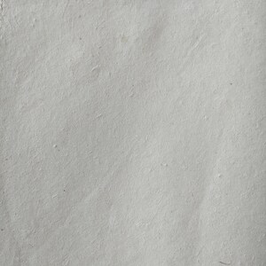 Op de afbeelding: Een close-up van een vel handgemaakt papier. Het papier is lichtgrijs van kleur met een licht getextureerd oppervlak. Het papier heeft een paar kleine imperfecties, waardoor het een natuurlijke uitstraling heeft.