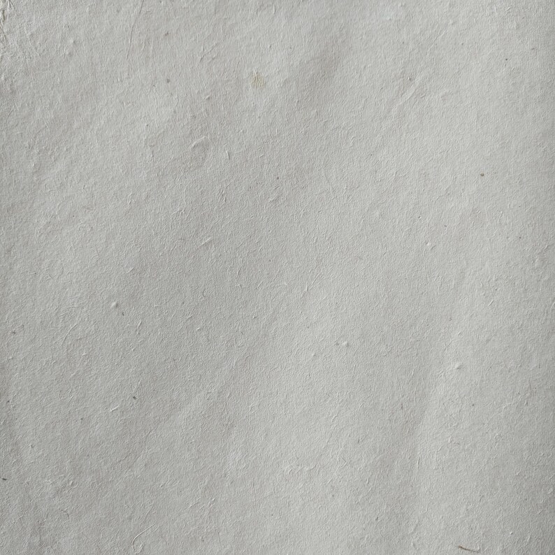 Op de afbeelding: Een close-up van een vel handgemaakt papier. Het papier is lichtgrijs van kleur met een licht getextureerd oppervlak. Het papier heeft een paar kleine imperfecties, waardoor het een natuurlijke uitstraling heeft.