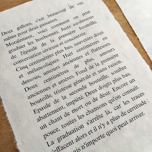 Puede incluir: Primer plano de un papel texturizado blanquecino con texto en franc&eacute;s impreso en tinta negra. El papel tiene un borde &aacute;spero e irregular. El texto parece ser un poema o un pasaje de un libro.
