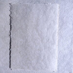 Pu&ograve; includere: Primo piano di carta fatta a mano con superficie strutturata e bordi irregolari. La carta &egrave; di colore bianco tenue, di forma rettangolare. Probabilmente utilizzata per arte o cancelleria.