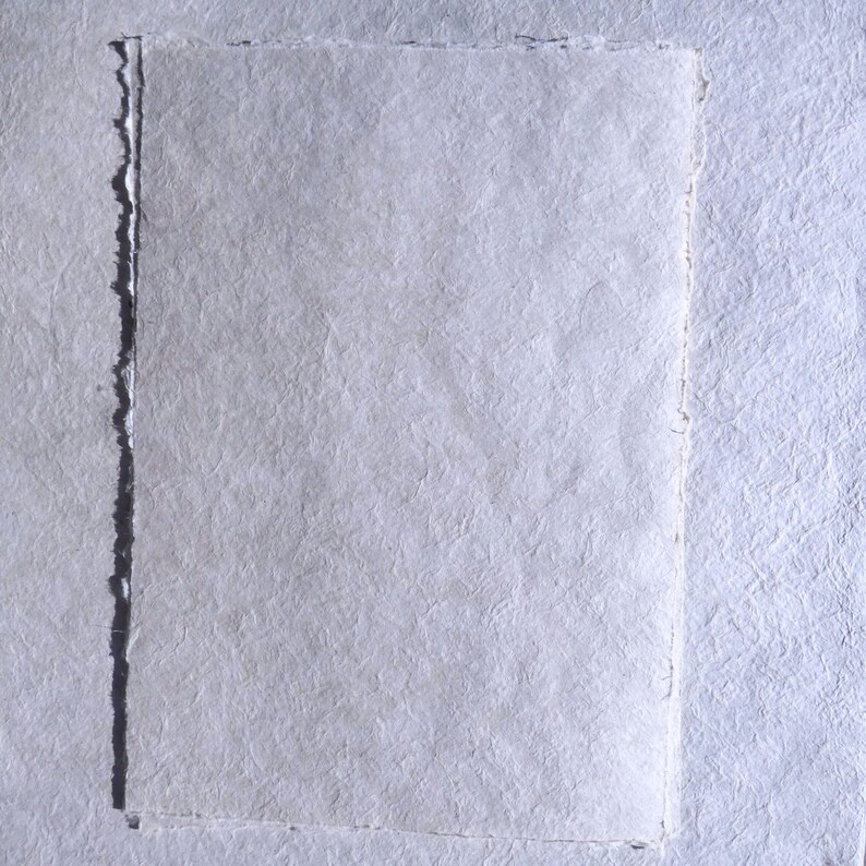 Pu&ograve; includere: Primo piano di carta fatta a mano con superficie strutturata e bordi irregolari. La carta &egrave; di colore bianco tenue, di forma rettangolare. Probabilmente utilizzata per arte o cancelleria.
