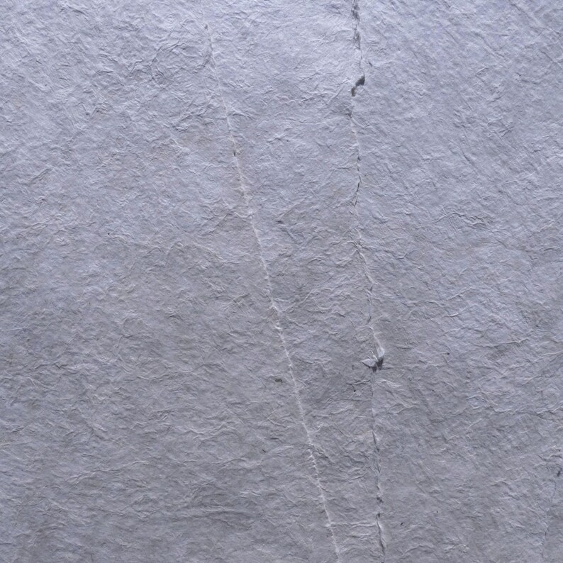 Pu&ograve; includere: Primo piano di un foglio di carta strutturata grigio chiaro. La carta ha un aspetto stropicciato con linee visibili e sottili variazioni di tono, suggerendo una qualit&agrave; fatta a mano o invecchiata. La superficie &egrave; illuminata in modo uniforme.