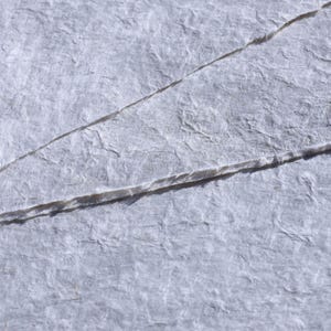 Pu&ograve; includere: Primo piano di carta strutturata grigio chiaro con fibre visibili e pieghe diagonali. La carta ha un aspetto ruvido e fatto a mano, suggerendo che potrebbe essere utilizzata per l'arte o l'artigianato.