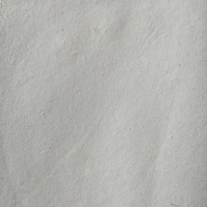 Puede incluir: Primer plano de una hoja de papel hecho a mano. El papel es de color gris claro con una superficie ligeramente texturizada. El papel tiene fibras visibles y sutiles variaciones de tono, lo que sugiere una calidad natural y org&aacute;nica.
