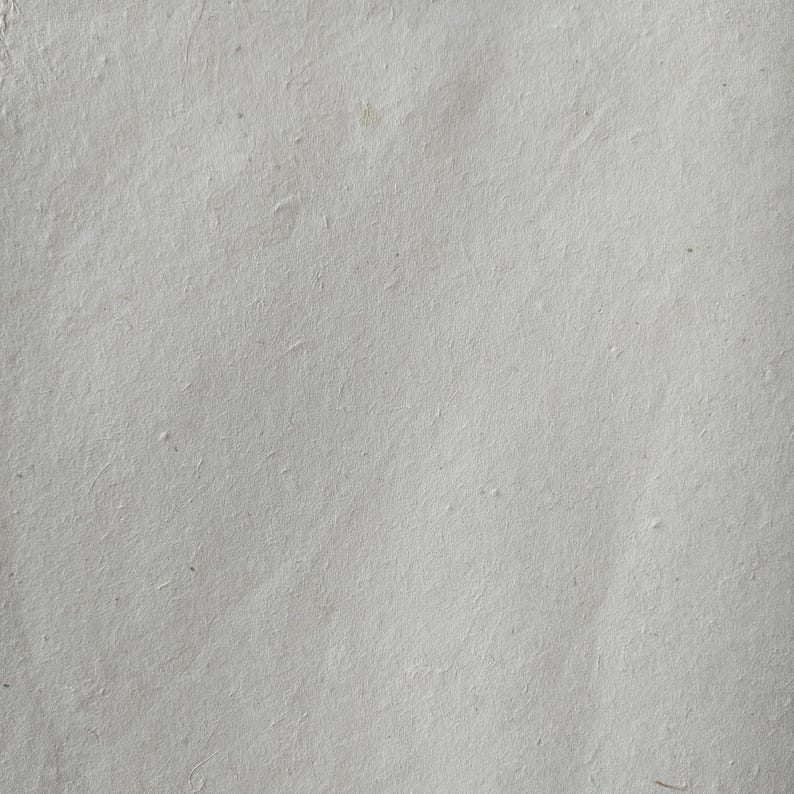 Puede incluir: Primer plano de una hoja de papel hecho a mano. El papel es de color gris claro con una superficie ligeramente texturizada. El papel tiene fibras visibles y sutiles variaciones de tono, lo que sugiere una calidad natural y org&aacute;nica.