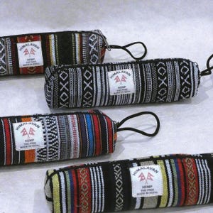 Puede incluir: Cuatro estuches cilíndricos de tela tejida con rayas verticales en negro, blanco, rojo, azul y amarillo. Cada estuche tiene una etiqueta rectangular blanca con el texto HIMALAYAN HEMP THC FREE MADE IN NEPAL y un tirador de cremallera negro.