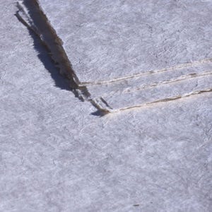 May include: Close-up of handmade paper with a textured, off-white surface. The paper has a deckled edge and appears to be layered. The paper has a subtle, natural texture, suggesting it is made from plant fibers.