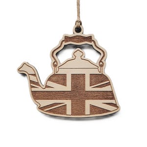 May include: A flat, laser-cut wooden ornament shaped like a teapot, featuring a natural light wood finish with a darker brown wood inlay depicting the Union Jack flag pattern. The ornament includes a small hole at the top with a jute twine loop.