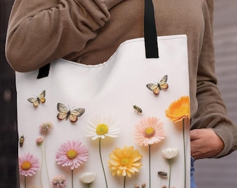 May include: A white tote bag with a floral design featuring pink, white, and yellow flowers, butterflies, and bees. The bag has black handles.