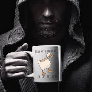 A spooky looking man, is holding a white ceramic mug in both hands that is hiding most of her face.  The mug features a funny looking goose with a baseball bat in it's mouth.  The caption reads "Mess with the honk, You get the bonk".  A funny silly goose gift idea, silly gift, gag gift, dad gift.