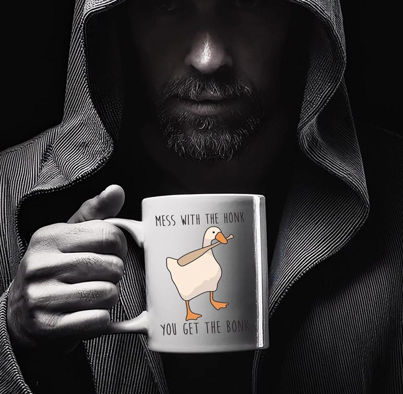 A spooky looking man, is holding a white ceramic mug in both hands that is hiding most of her face.  The mug features a funny looking goose with a baseball bat in it's mouth.  The caption reads "Mess with the honk, You get the bonk".  A funny silly goose gift idea, silly gift, gag gift, dad gift.