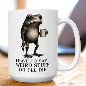 May include: White ceramic mug featuring a detailed illustration of a frog holding a small coffee cup. The frog has a serious expression. Text on the mug reads: "I HAVE TO SAY WEIRD STUFF OR I'LL DIE."