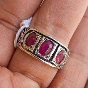 Peut inclure: Une bague en argent avec trois pierres précieuses ovales rouges serties dans des montures en argent ornées.