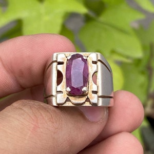 May include: A silver ring featuring a large, oval-shaped, dark pink gemstone set within a decorative, silver frame.