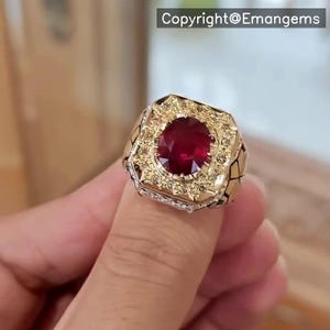 Könnte beinhalten: Ein goldener Ring mit einem großen roten Edelstein, der von kleineren gelben Edelsteinen umgeben ist. Der Ring hat eine strukturierte Band.