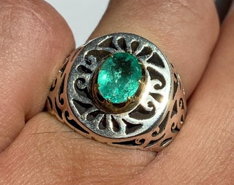 May include: A silver ring with an ornate design and a large, oval-shaped emerald gemstone set in the center.