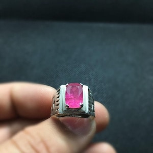 Peut inclure: Une bague en argent avec une pierre précieuse rose sertie dans une bélière rectangulaire. La bague a une bande texturée.