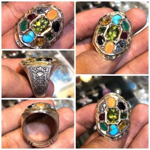 May include: A silver ring with a large green gemstone surrounded by smaller gemstones in various colors, including turquoise, red, and yellow.