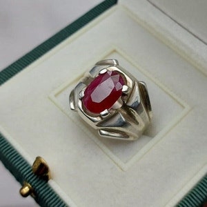 Peut inclure: Une bague en argent avec une grande pierre précieuse de rubis de forme ovale sertie dans un motif géométrique.
