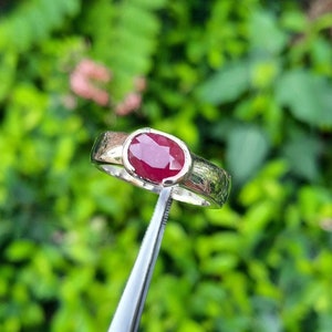 Peut inclure: Une bague en argent avec une pierre précieuse ovale rouge sertie dans un sertissage à bélière.