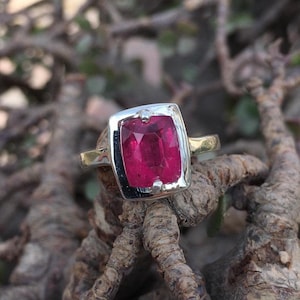 May include: A silver ring featuring a square pink gemstone set in a bezel setting.