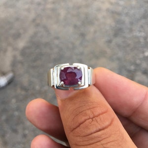 Puede incluir: Un anillo de plata con una gran piedra preciosa de rubí rojo oscuro de forma cuadrada.